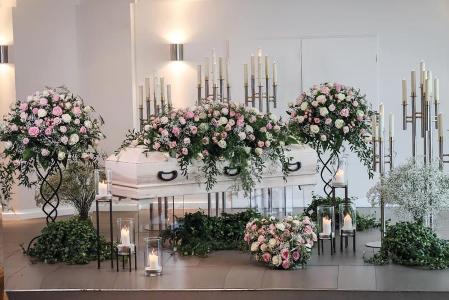 Ein weißer Sarg steht in einem hellen Raum der mit Blumen und Kerzen geschmückt ist