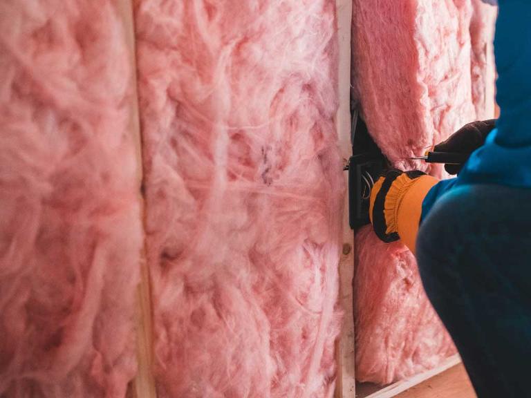Ein Mensch steckt rosafarbenes Isoliermaterial in eine Zwischenwand