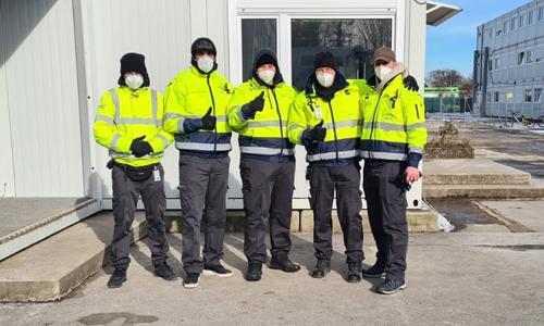 Fünf Mitarbeiter in Sicherheitskleidung mit Mund- Nasenmaske zeigen den Daumen nach oben.