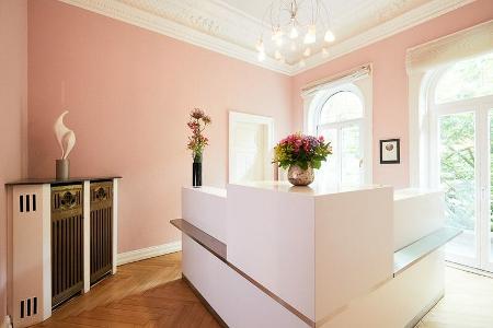 Der Empfang in der Praxis, ein weißer Tresen vor einer rosafarbenen Wand und großen weißen Fenstern