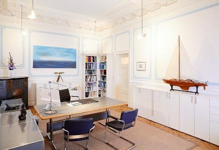Ein Besprechungszimmer mit einem Schreibtisch und Stühlen davor, ein Holzfußboden und weiße Wände