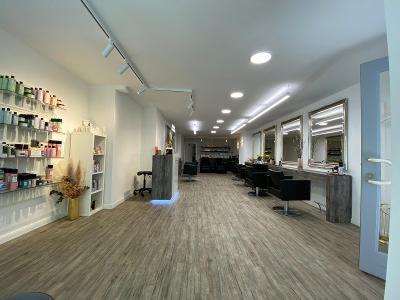 Dimen Soreni Hairdesign Geschäft von innen, weiße Wände, Deckenbeleuchtung und Holzfußboden, rechts sind Spiegel an den Wänden und davor stehen schwarze Sessel