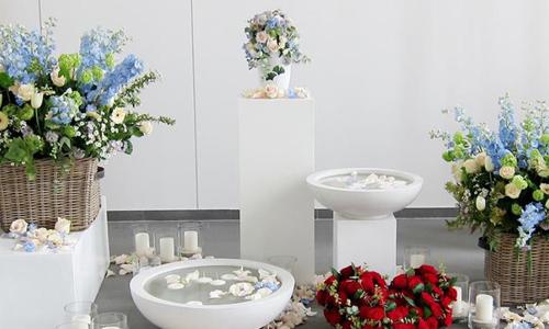 Ein Raum mit weißen Wänden, einem grauen Fußboden und weißen Säulen mit Blumendeko darauf, davor und auf dem Boden liegend