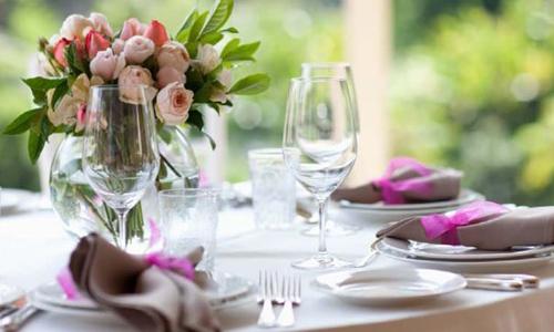 Ein Tisch mit weißer Tischdecke, einer Glasvase mit Tulpen darin, Teller und Besteck darauf liegend
