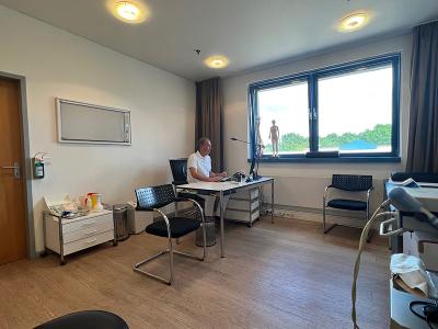 Das Behandlungszimmer von Dr. med. Axel Zimmermann, Fensterfront und ein Schreibtisch mit Stuhl