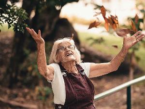 Ältere Dame steht im Garten und reißt die Arme in die Luft.