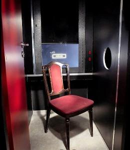 Ein roter Stuhl in einer Kabine mit einem Loch in der Wand