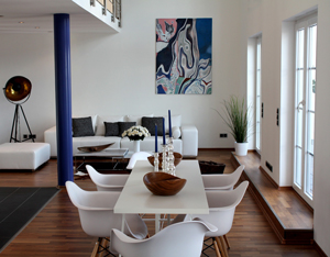 Ein Raum mit einem langen Tisch und Stühlen daran, im Hintergrund ein weißes Sofa und Kunst an der Wand