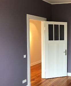 Eine graublaue Wand, ein Holzfußboden und eine weiße Tür