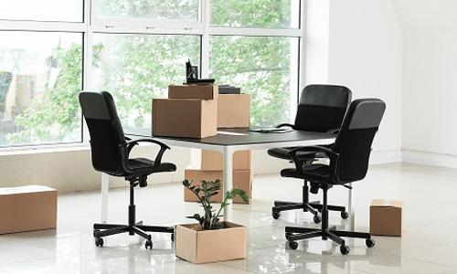 Drei schwarze Bürostühle stehen um einen Tisch auf dem Kartons stehen