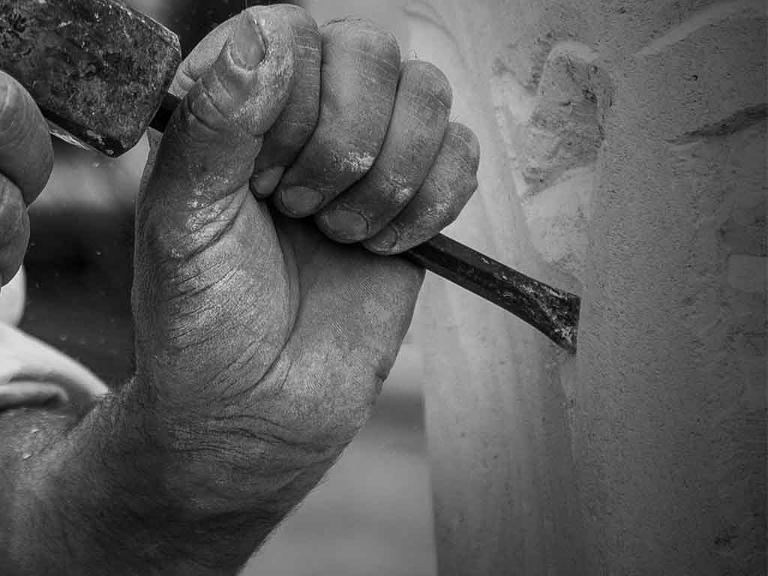 Mit Hammer und Meißel wird an einem Stein gearbeitet.