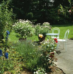 Ein weißer Tisch und zwei Stühle stehen auf Steinplatten in einem Garten