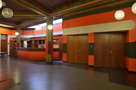 Eine Eingangshalle mit orangefarbenen Wänden, dunklen Holztüren und runden Lampen an der Decke