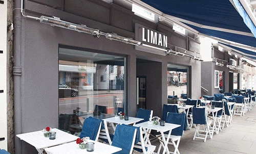 Außenterrasse von Liman mit weißen Tischen und blauen Stühlen
