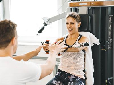Ein Mann unterstützt eine Frau bei Trainingsübungen an einem Fitnessgerät