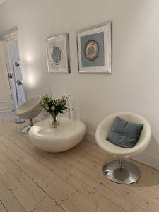 Zwei Sessel stehen neben einem Tisch vor einer weißen Wand mit zwei Bildern und auf einem hellen Holzfußboden