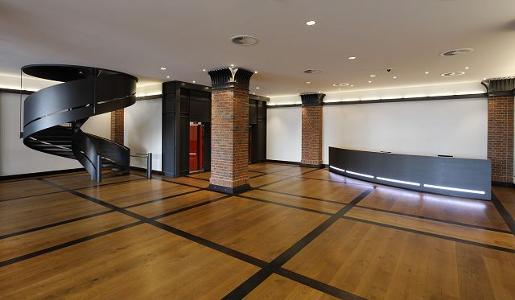 Ein Raum mit dunklem Holzfußboden, Säuen aus rotem Backstein und einer schwarzen Wendeltreppe
