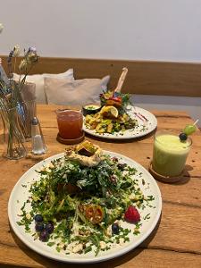 Zwei weiße Teller mit Salat auf einem Holztisch und jeweils einem Getränk daneben