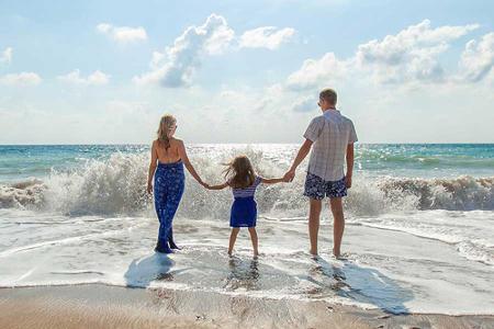 Eine Frau, ein Kind und ein Mann halten sich an den Händen und stehen im Wasser an einem Strand