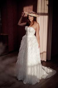 Eine Frau in einem weißen Brautkleid mit einem Hut auf, wird von der Sonne angestrahlt