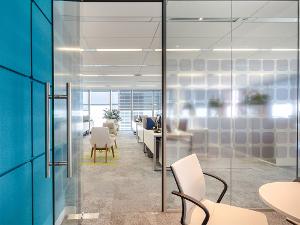 Der Blick aus einem Besprechungsraum mit Wandverglasung in ein großes, helles Büro