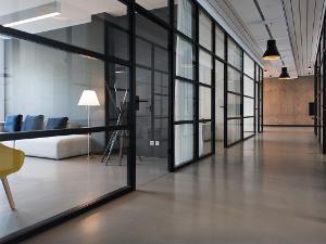 Ein grauer Flur und links und rechts gehen gläserne Büros ab mit schwarzen Rahmen