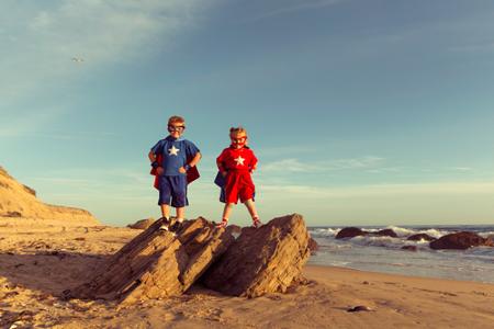 Zwei Kinder in einem Supermannkostüm stehen auf einem Felsen am Strand
