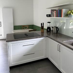 Eine helle Küche mit weißen Schränken und grauer Arbeitsplatte, grauem Fliesenboden und Spritzschutz an der Wand