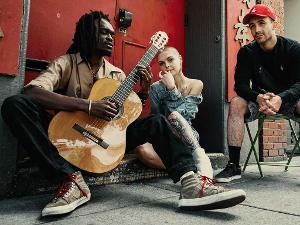 Drei Menschen sitzen zusammen auf der Straße, einer spielt Gitarre und die anderen beiden hören zu