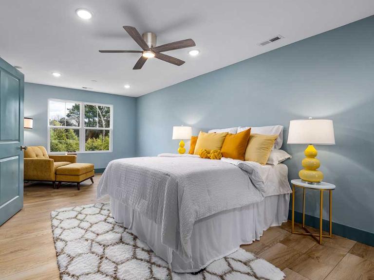 Ein Raum mit hellblauen Wänden, einem hellen Holzfußboden und einem Bett mit heller Bettwäsche und gelben Kissen sowie gelb-weißen Nachttischlampen
