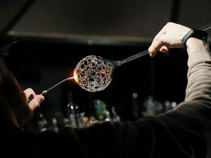 Ein Glasbläser bearbeitet und erstellt eine Runde Glaskugel mit Löchern