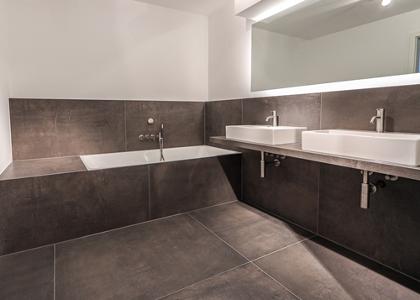 Ein Badezimmer mit grauen Fliesen und einem großen Spiegel über den Waschbecken