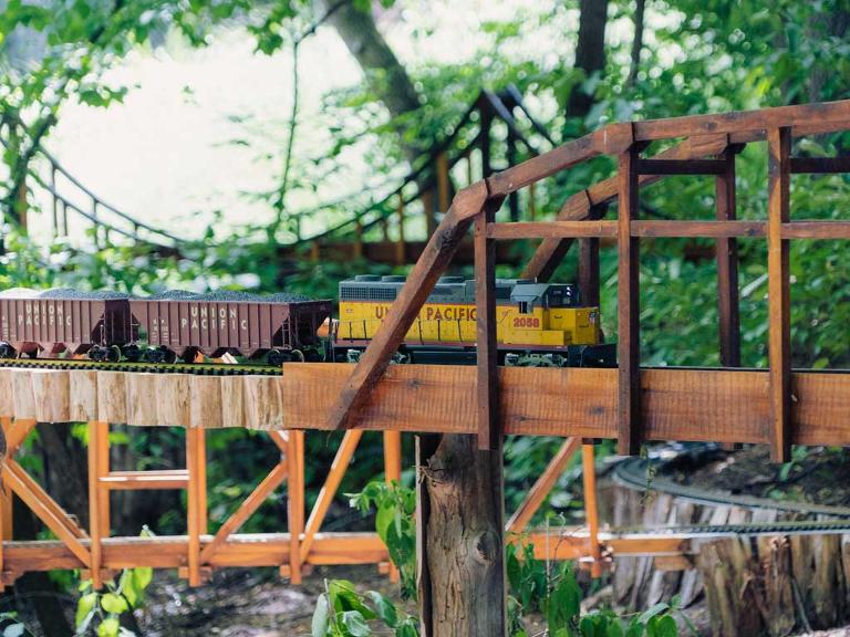 Ein Modell einer Eisenbahn fährt über eine selbstgebaute Holzbrücke im Grünen