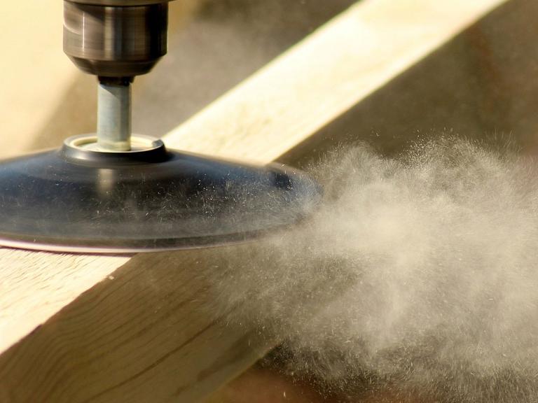 Eine Schleifmaschine an einem Stück Holz wirbelt Späne auf
