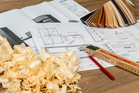 Ein Bauplan, ein Bleistift, ein Zollstock, ein Farbfächer und Sägespäne auf einem Holztisch