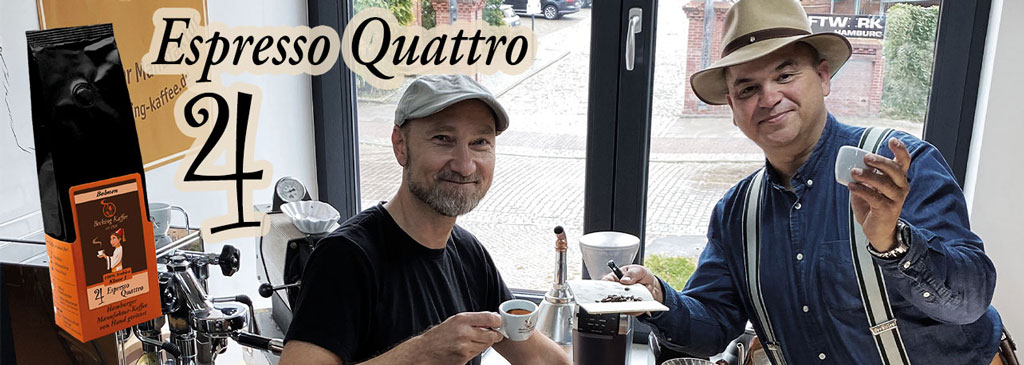 Zwei Männer trinken jeweils einen Espresso, stehen vor einem Fenster und lächeln in die Kamera