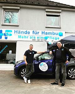 Zwei Mitarbeiter von Hände für Hamburg stehen an einem Auto gelehnt vor dem Büro.