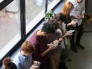 Menschen schauen auf ihr Handy und lehnen an einem Fenster