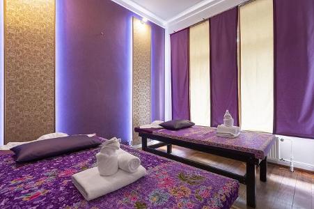 Ein Raum mit zwei Massageliegen und lila sowie goldfarbenen Wänden und Vorhängen