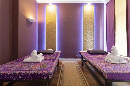 Zwei Massageliegen mit Blumenauflagen in einem lila gestrichenen Raum mit zwei goldenen Streifen an der Wand