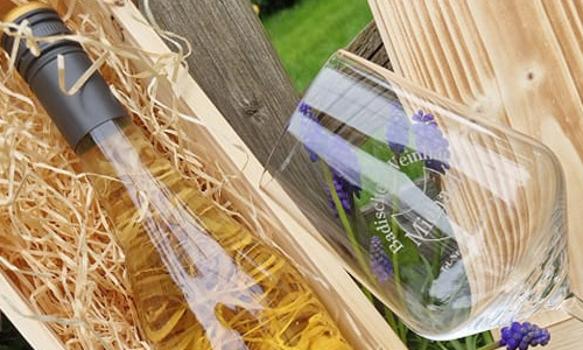 Eine Weinflasche in einem Holzkarton mit Stroh und einem Weinglas daneben