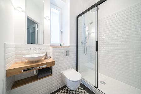 Ein weiß gefliestes Badezimmer mit einer Dusche mit Glaswand, einem Waschtisch aus Holz und einem kleinen Fenster