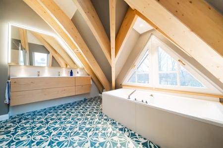 Ein Badezimmer unter dem Dach mit Dachbalken, einer Badewanne, einem Waschtisch aus Holz und einem türkisfarbenem Fußboden