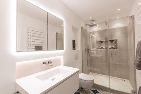Ein Badezimmer mit Spiegel über dem Waschbecken, einer Dusche mit Glaswand und grauen Fliesen