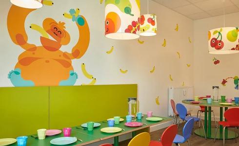 Ein Raum mit einem orangefarbenen Affen und gelben Bananen an der Wand, bunte Stühle und Tische stehen davor