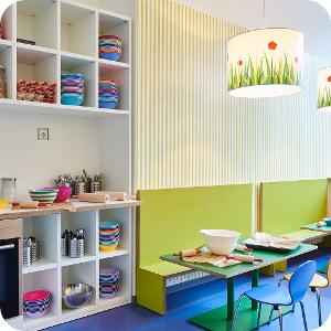 Der Raum zum Essen in der Kita kinderzimmer City Süd mit bunten Stühlen, Tischen und Deckenlampen