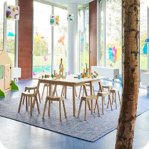 Ein heller Raum in der Kita kinderzimmer City Süd mit Holzgestühl, bodentiefen Fenstern die mit bunten Bildern beklebt sind