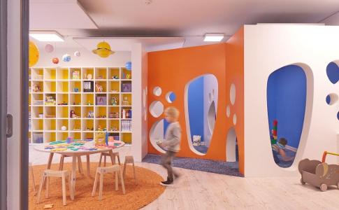 Ein Spielzimmer der Kita kinderzimmer ConventParc, mit blauen, gelben und orangefarbenen Akzenten, einem Bücherregal und einem Tisch mit Stühlen sowie einem runden Teppich
