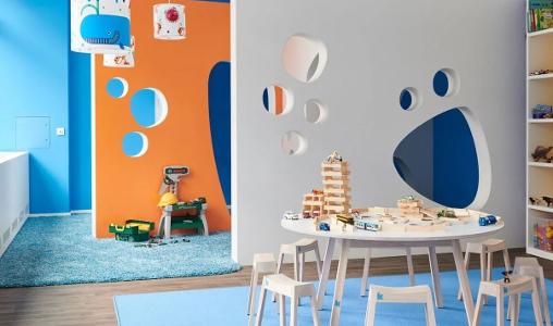 Abgetrennte Räume in der Kita kinderzimmer Hammerbrook mit orange, blau und weißen Wänden, blauem Teppich und eine Holztisch mit Stühlen