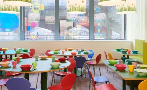 Der Raum zum gemeinsamen Essen in der Kita kinderzimmer Hammerbrook, bunte Tische und Stühle vor einer Fensterfront